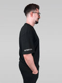 Mann im schwarzen Buy Oil Shirt von der Seite, Bibelvers auf dem Ärmel