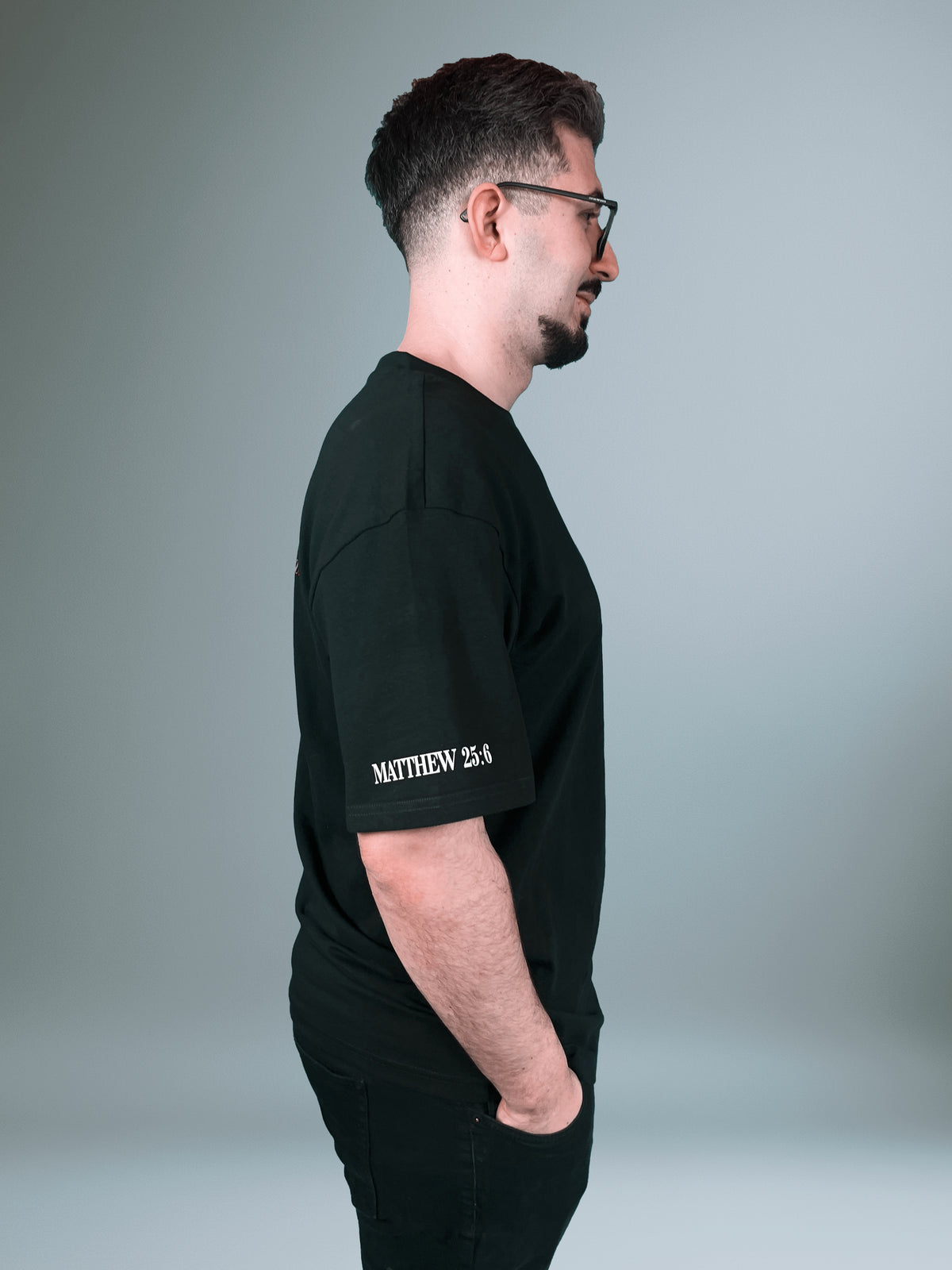Mann im schwarzen Buy Oil Shirt von der Seite, Bibelvers auf dem Ärmel