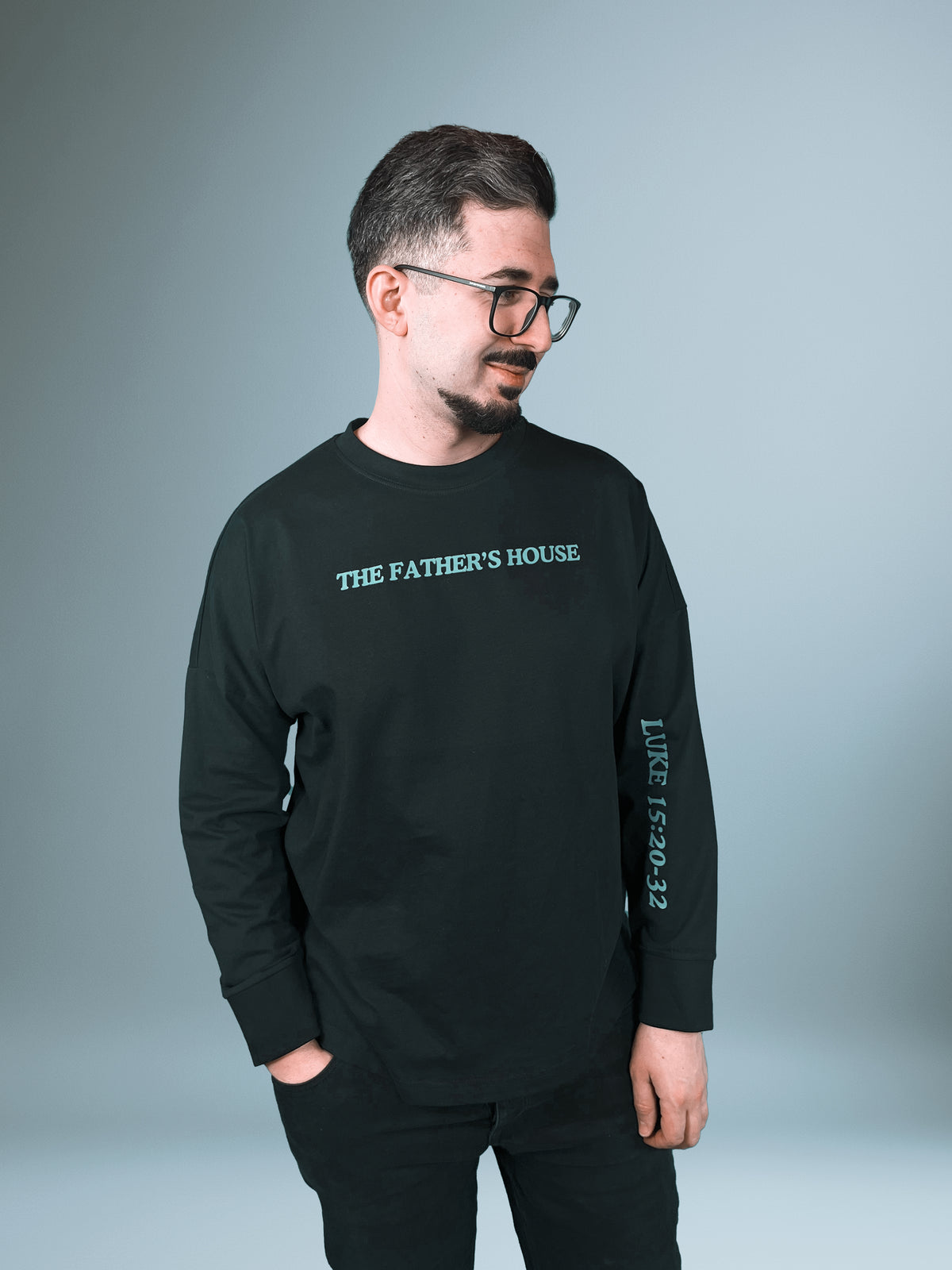 Mann im schwarzen Father's House Longsleeve mit Lukas 15,20-32 auf dem Ärmel